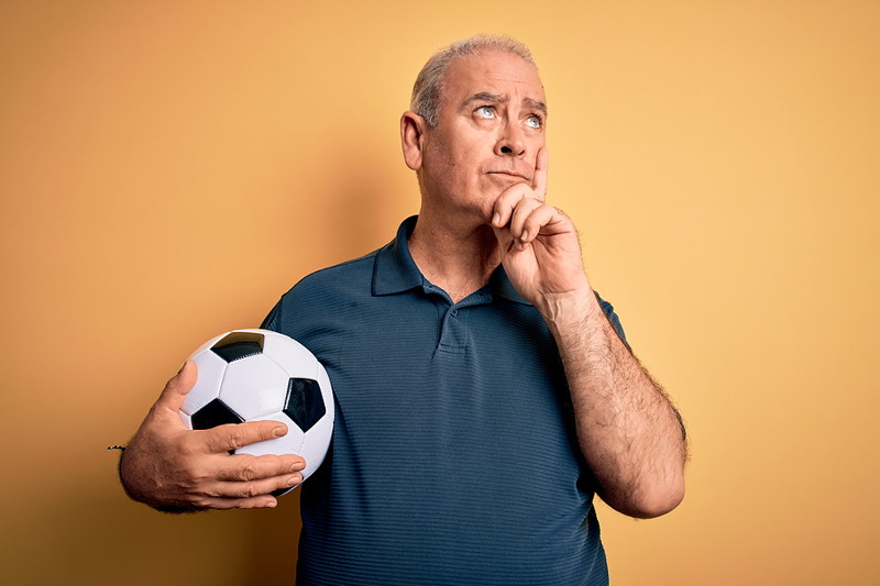 older man holding football thinking